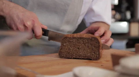 Cook cuts a slice of bread on a cutting board with a knife Видео 58861254