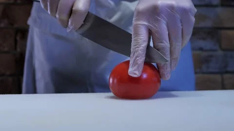 Cook cuts the tomato into slices with a large kitchen knife Stock-Footage 131077784