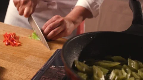 Cook cuts vegetables to add them to edible burdock in a pan Stock Footage 119189848
