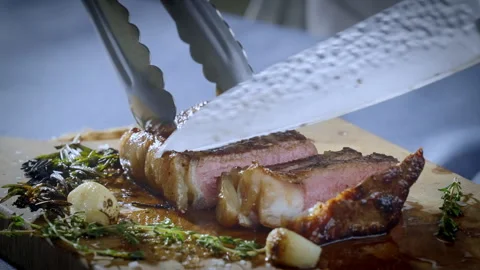 The cook cutting the steak with a large kitchen knife on a cutting board. Stock Footage 263492297