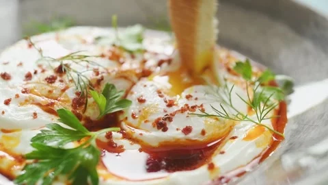 The cook dips a slice of bread into the freshly made turkish eggs. Video stock 207024113