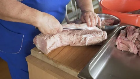 A cook in a field kitchen cuts pork on wooden cutting board. Hand-held camera Stock Footage 153154487