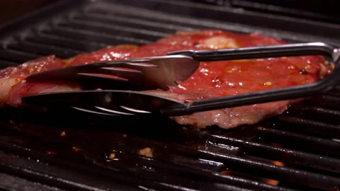 Cook flips the delicious steak on the surface of the grill with a kitchen tongs Stock Footage 136480823