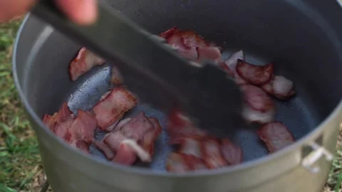 Cook frying thin slices of bacon on a hot pan and stirring them with a spatula. 스톡 동영상 334643407