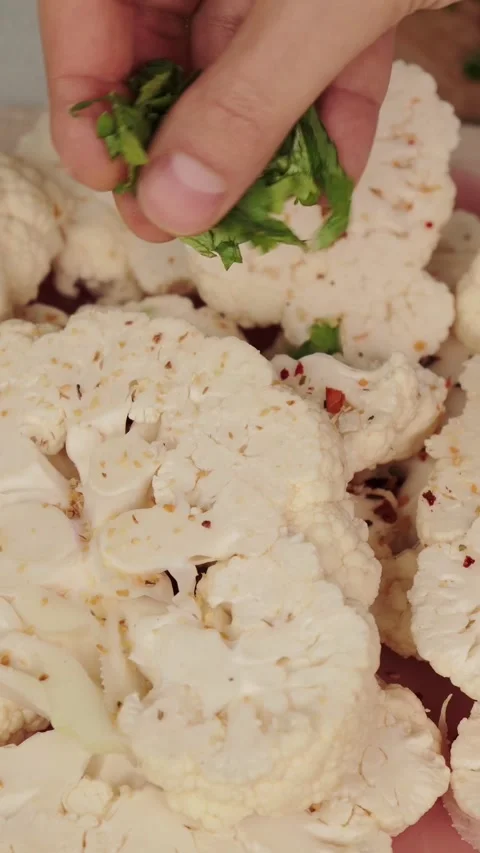 Cook garnishing fresh raw sliced cauliflower steaks with chopped green herbs and 스톡 동영상 346774441