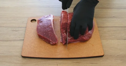 Cook in gloves cuts beef meat with a knife on a board and makes steaks 動画素材 123563468