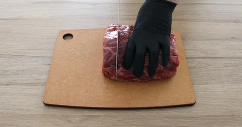 Cook in gloves cuts beef meat with a knife on a board and makes steaks ribeye 動画素材 125433820