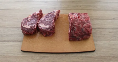 Cook in gloves cuts beef meat with a knife on a board and makes steaks ribeye 動画素材 125433885