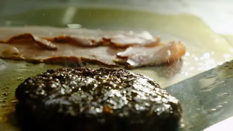 Cook in gloves uses spatula to flip sizzling hamburger patty 動画素材 325025623
