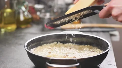 The cook grating parmesan cheese on risotto with mushrooms in the frying pan. Stock Footage 154370609