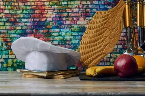 Cook hat,Chef's cap on a fruit table with a carved board with colored bricks  Stock Photos