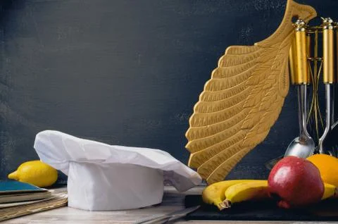 Cook hat,Chef's hat on a table with fruit carved board and dark background of Stock Photos