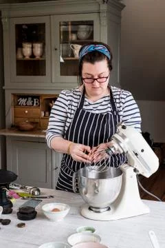 A cook in her kitchen breaking eggs and weighing ingredients for chocolate Stock Photos
