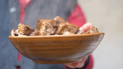 Cook holds in his hands an earthenware dish of fried pieces of beef liver Stock Footage 125696251
