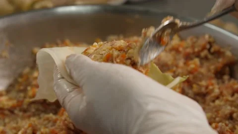 The cook holds the stuffed cabbage and pours a spoonful of minced meat into it. Video stock 150448101