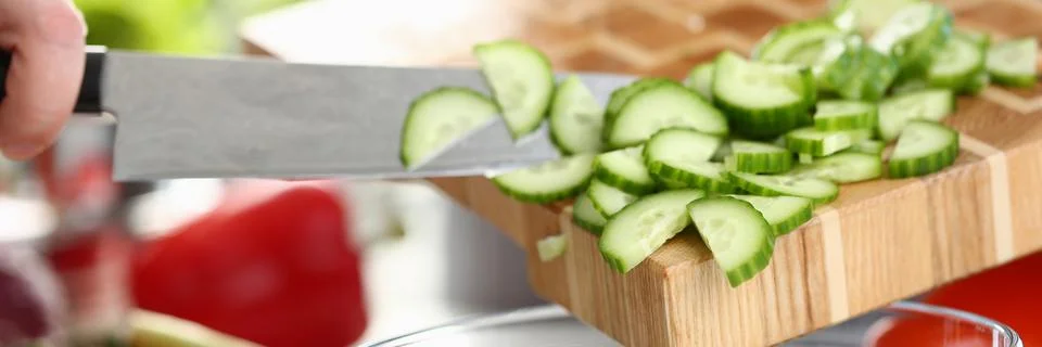 Cook in kitchen at work prepares vegetable salad and cuts green cucumber Stock Photos