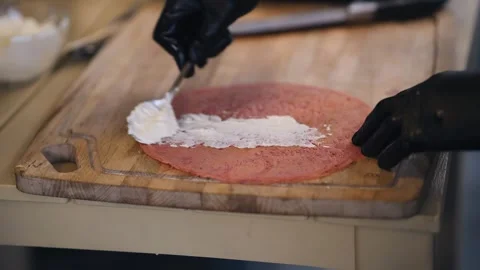 The cook makes a meat pizza on the table. He puts the sauce on the meat base Stock Footage 249261556