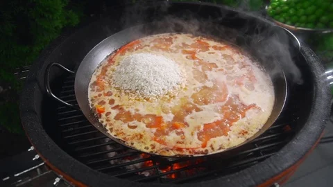 The cook makes paella on the open fire and adds green pea to the other Stock Footage 77549506