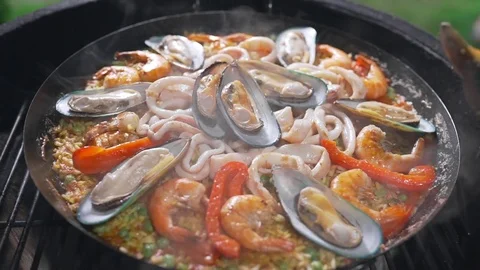 The cook makes paella on the open fire in the big hot pan, grill anf barbecue Stock Footage 77550046