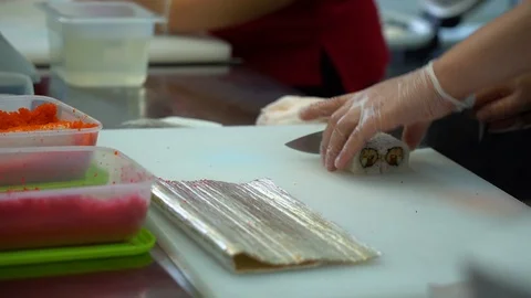 Cook man in white gloves cuts sushi rolls with knife on a white table in kitchen Stock Footage 119978971