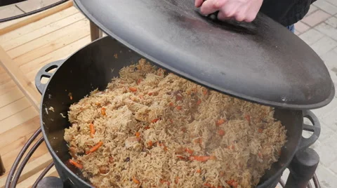 Cook opens a lid of big kettle with a delicious pilaf on Street Food Fair Stock Footage 61345432