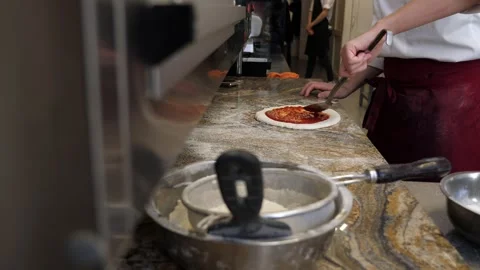 Cook or baker with spoon applying tomato sauce to raw pizza dough at pizzeria. Stock Footage 308001766