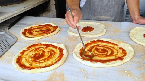 Cook or baker with spoon applying tomato sauce to raw pizza dough at pizzeria. Video stock 311018739