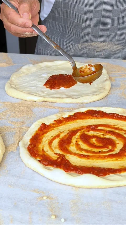 Cook or baker with spoon applying tomato sauce to raw pizza dough at pizzeria. Stock Footage 311067163