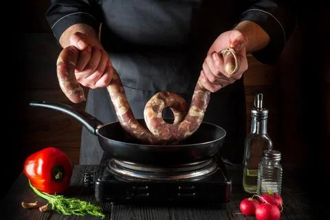 The cook or chef puts raw meat sausage into the pan before cooking. Stock Photos