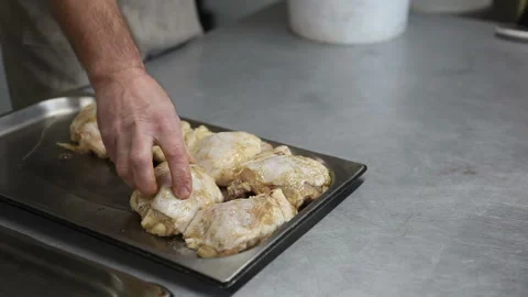 The cook places chicken legs on a baking sheet to be cooked in a combi steamer Stock Footage 320300301