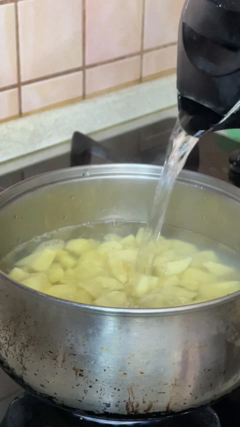 Cook pouring boiling water into a pot with raw potatoes on the stove Stock Footage 272157795