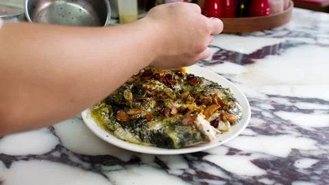 Cook Pouring Sauce Over Cooked Fish with Garlic and Herbs on Marble Kitchen Stock Footage 337652954
