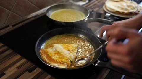 Cook pours orange sauce over folded pancakes fried in a frying pan Stock Footage 233992393