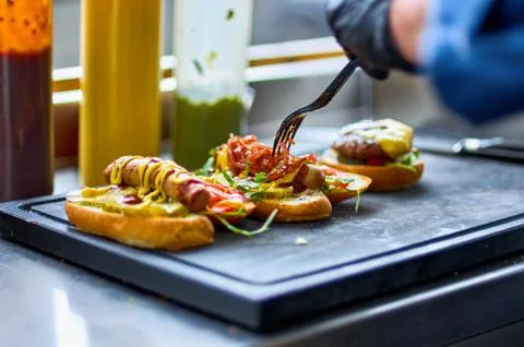 The cook prepares a hot dog, adding the sauce to the sausage. Two hamburgers, Stock Photos