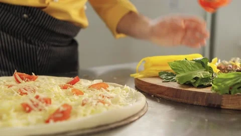 Cook prepares pizza. Puts red pepper, cheese, tomatoes Video stock 130562564