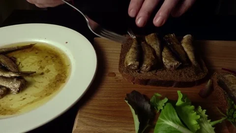 The cook prepares a sandwich on a black bread with sprats Stock Footage 74238312
