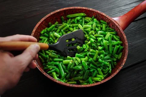 The cook prepares the side dish. Mixing green string beans in a frying pan Stock Photos