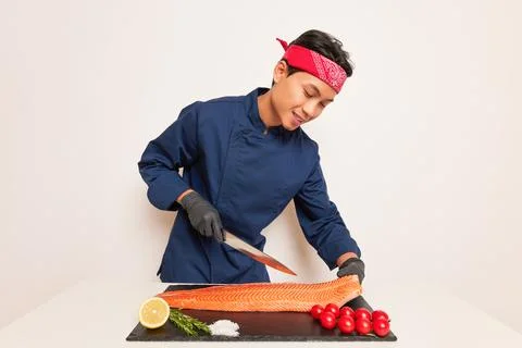 A cook preparing to slice salmon for some meal, working at the table in the Stock Photos