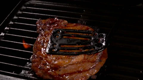 Cook presses the steak to the hot surface of the grill with a black spatula Stock Footage 136455723