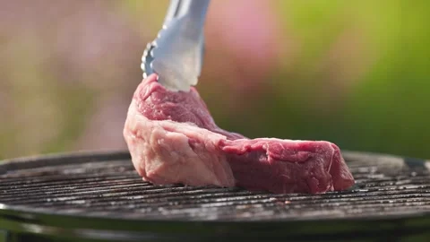 A cook put fresh raw beef steak on charcoal grill in backyard garden for maki Stock Footage 315995524
