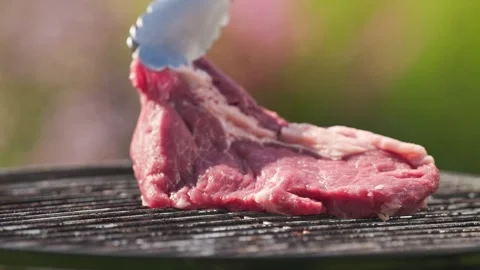 A cook put fresh raw beef steak on charcoal grill in backyard garden for maki Stock Footage 315995588