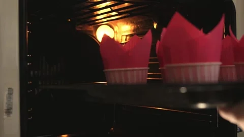 The cook puts a baking sheet with sweet cupcakes inside the hot electric oven Stock Footage 149029053