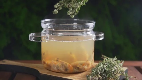 The cook puts bunch of thyme to the hot shrimp broth in the glass pan standing Stock Footage 77547780