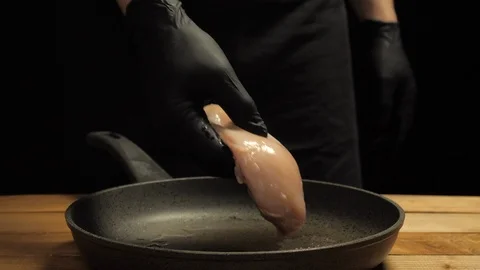 Cook puts gloved chicken fillet on a hot frying pan Stock Footage 107724012