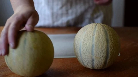 A cook puts on a old wooden table a cutting board and two ripe melons. Stock Footage 126322262