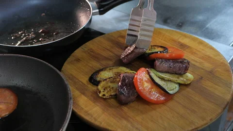Cook puts pieces of beef and grilled vegetables on a wooden stand. Stock Footage 131077944