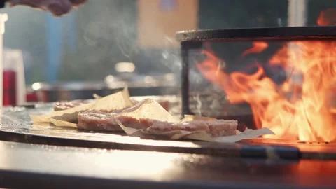 Cook puts raw burger cutlet on craft baking paper over flaming grill. Video stock 346404034
