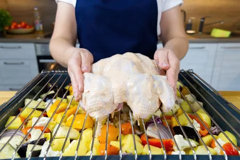 The cook puts the raw chicken on a baking sheet with vegetables. The process of Stock Photos
