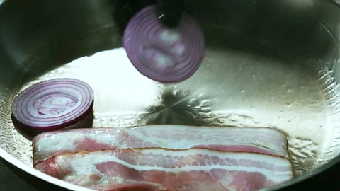 Cook puts sliced red onion rings on a hot pan with bacon Stock Footage 101750506