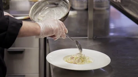 The cook puts spaghetti on a plate and sprinkles with ground pepper Stock Footage 76004307